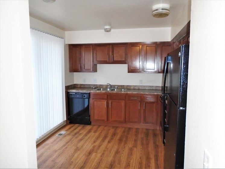 A kitchen with brown cabinets, white walls, dishwasher, sink, stove, and refrigerator